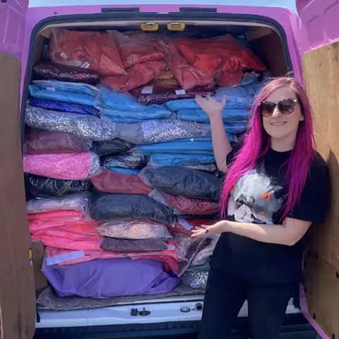 Ally Outten/PA Media A woman with long purple hair showing prom dresses in the back of a van. Ally wears sunglasses and a black t-shirt and jeans. 