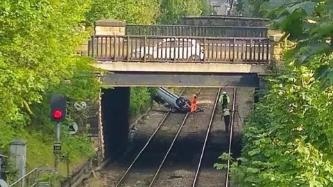A silver car overturned on railway tracks.