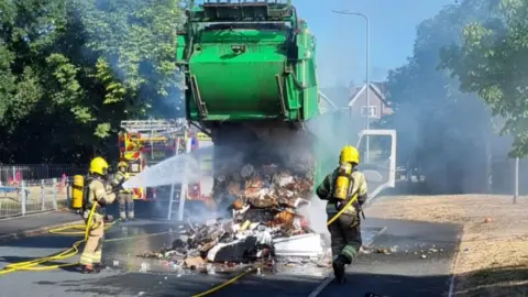 Herefordshire Council Firefighters put out a fire on pile of a rubbish a bin lorry in the middle of the road.