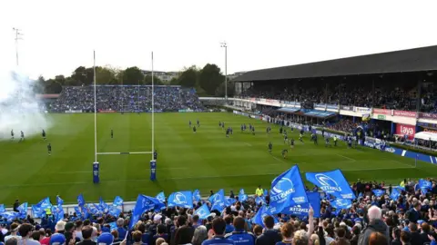 Leinster fans wave blue flags as smoke from fireworks drifts across their home ground ahead of a game against Connacht in 2024