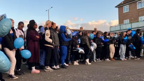 Sam Read/BBC A line of people mainly in coats holding balloons - many of which are blue