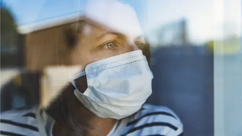 Getty Images woman wearing mask looking out of window