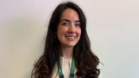 A woman with long brown hair, smiling at the camera.