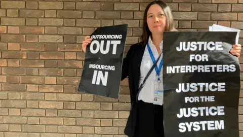 Henry Godfrey-Evans/BBC Protester holding up her signs in front of a court