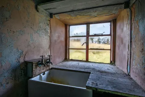 Angus Mackay Photography There is a small window above a small, stone sink. Two taps stick out from a wooden box above the sink.