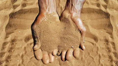 Close-up overhead view of the wrist and hands of an adult male cupping the golden sandy soil of Limpopo Province, South Africa.