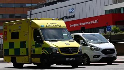 Yellow London Ambulance Service ambulance parked outside an NHS hospital emergency department (A&E).