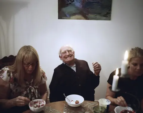 Sian Davey An old man laughs around his family.