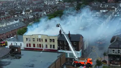 Kevin Haworth Drone aerial image of a fire on Lord Street, Fleetwood, as firefighters tackle the blaze. There are three fire engines and an aerial platform at the scene. Smoke is seen billowing from the roof of the three-storey building.