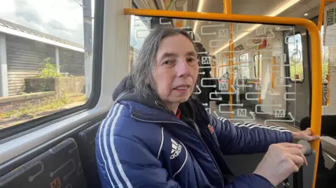 Paula Mitchinson is travelling on a new Tyne and Wear Metro train. She is sitting and holding her walking cane. 
