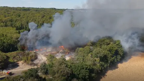 Smoke billowing from a fire at a yard surrounded by woodland