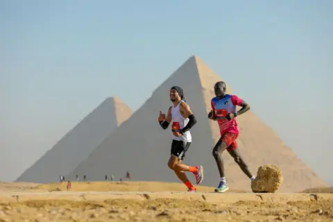 Mohamed Elshahed/Getty Images Two runners run side by side during the Maraquez Pyramid Half Marathon in Giza, Egypt's largest city - Saturday, December 14, 2024