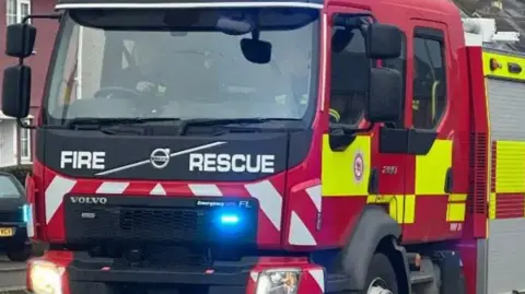 The front of a fire and rescue vehicle on the road with two firefighters sat in the seats.
