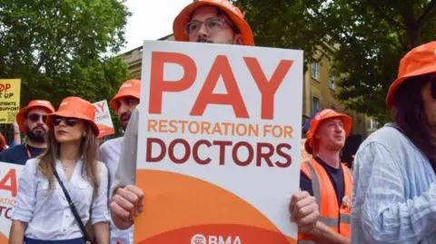 A person at a strike holds a poster which reads: "Pay restoration for doctors."