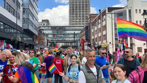 Crowds of people in Birmingham celebrating Pride in 2024. Several people hold Pride flags.