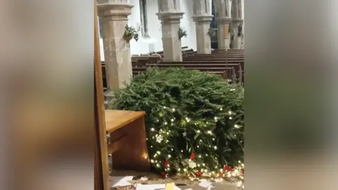 Contributed Another view of one of the Christmas trees that was torn down. Its lights and decorations lie around the floor after having fallen off. Pews are lined behind the tree.