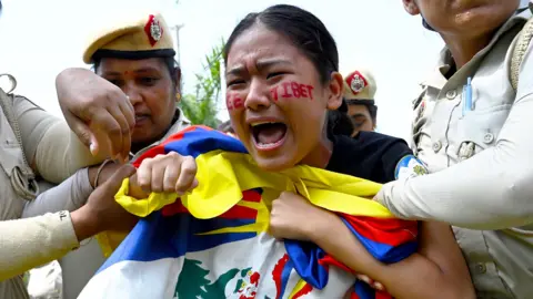 A woman with Free Tibet written on her face and carrying the Tibetan flag cried out as she is detained by female police offers in India 