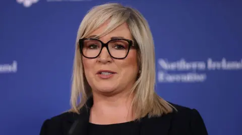PA Media Michelle O'Neill has blond hair to her shoulders and black framed glasses
