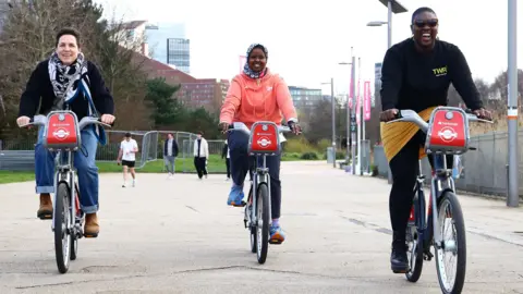 TfL Three women, who had bikes named after them are cycling towards the camera while smiling and laughing.