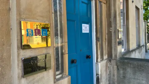 The exterior blue double doors of the BLB Solicitors office in Trowbridge. There is a gold sign to the left of the doors and a piece of paper attached to the doors which reads 'our reception is closed today - please ring office for assistance'.