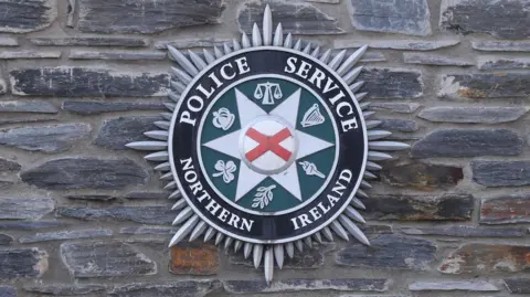 Police Service of Northern Ireland badge on a grey stone wall.