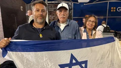 Max Radford and his mother and father pose for a picture, holding the flag of Israel, after landing in Birmingham 