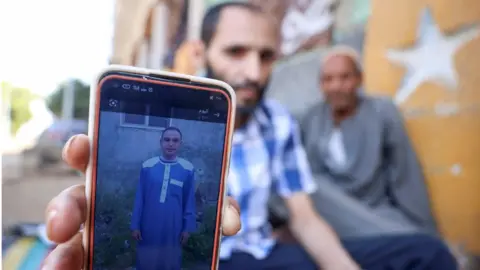 Reuters A man shows a photo of his brother Aly, who died along with his three cousins in Libya after Storm Daniel hit the country