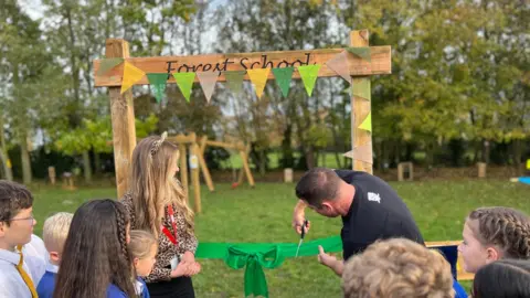 Kate Bradbrook/BBC Mrs Charley Oldham (left) and Steve Backshall cutting a ribbon to open the forest school