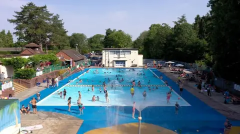 Handout A view of the lido, which opened in 1935 and has been restored. There are people swimming in the pool and standing around it on a sunny day.