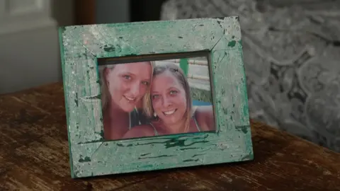 Family handout A photograph of Catherine and Annabel from when they were younger, inside a green wooden frame, sits on top of a coffee table. They both have blonde hair, are wearing summer clothes and are smiling.