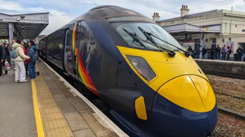Getty Images A high-speed Javelin train with rainbow livery stands at the platform of Canterbury West Station as passengers wait to board under a cloudy sky