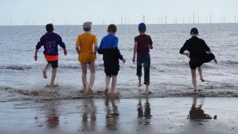 Five boys running into the sea in Skegness with their backs to the camera. 