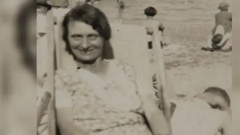 Louisa Dunne sitting in a deck chair facing the camera with other people in the background.