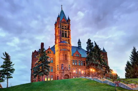 Getty Images A grand, 19th Century sandstone building, with a tower at the front. It sits on top of a hill and it is lit up against a dark grey cloudy sky. There are a lot of steps up to the building, which is surrounded by half-a-dozen trees,