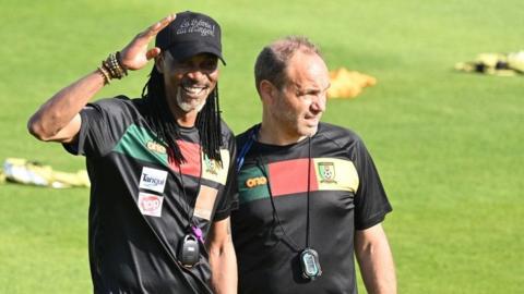 Rigobert Song and Sebastien Migne stand in the sunshine at a training session