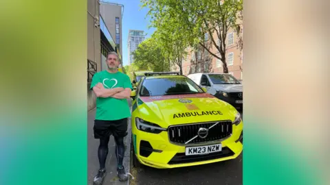 Stuart stands in front of an ambulance car with his arms crossed