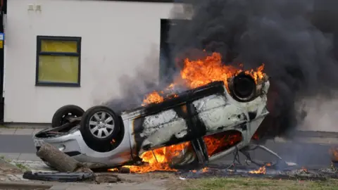 An upturned car on fire in front of a residential house in Middlesbrough