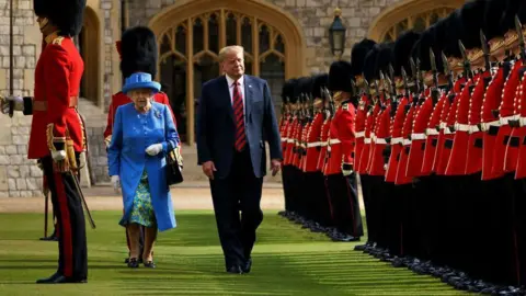 O AFP Donald Trump caminha ao lado de Elizabeth, a segunda rainha Elizabeth no castelo de Windsor através da imagem de Gatety, em um terno azul e gravata vermelha. Ele usa um casaco de terno azul brilhante e um chapéu combinando. Eles vestindo o tradicional casaco militar vermelho, calça preta e chapéu preto de flafie por guardas reais.