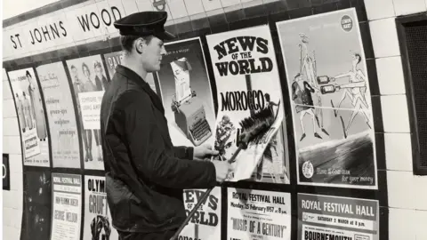 TfL A uniformed man putting up posters in St John's wood underground station