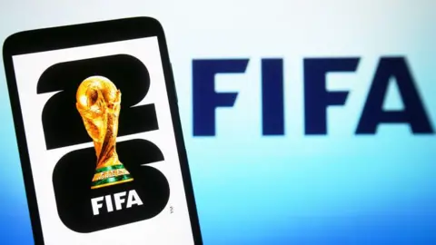 In this illustration, a World Cup 2026 logo is shown on a smartphone screen in front of a Fifa logo