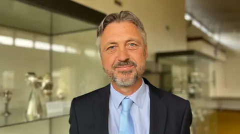 A head-and-shoulders picture of a man with a beard in a suit and tie