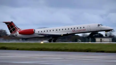 A long white plane taking off from a runway. There's a green strip of grass in the background.
