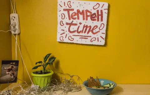 BBC Polystyrene sign with 'Tempeh Time' painted on it in red above a bowl of food, on a bright yellow wall