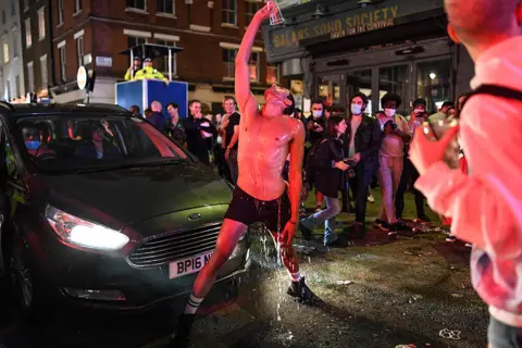 Peter Summers/Getty Images A man pours a drink over himself in the street