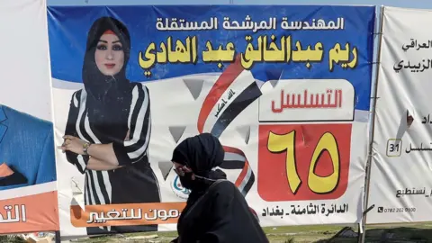 An Iraqi woman walks next to election campaign posters for candidates in Baghdad, Iraq (5 October 2021)