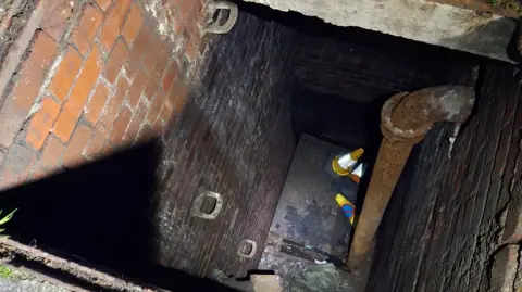 Devon and Somerset Fire and Rescue Service A view from the top of a drain looking down. There is a metal pipe on the right and traffic cones at the bottom.