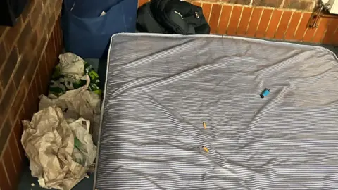 A dirty mattress is on the floor of the communal room with lighters and cigarettes 