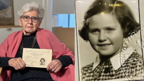 An elderly woman holding up her child identity card alongside a picture of her as a child 