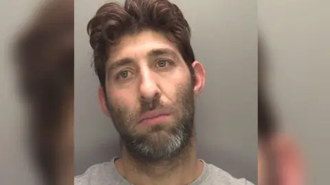 Lincolnshire Police A police mugshot of Maksim Iliev. He has short brown hair and a dark brown, trimmed beard, with white flecks, and is wearing a grey t shirt.