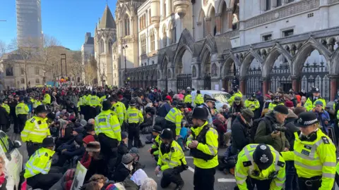 Large numbers of police speak to protesters sitting on the Strand outside Royal Courts of Justice